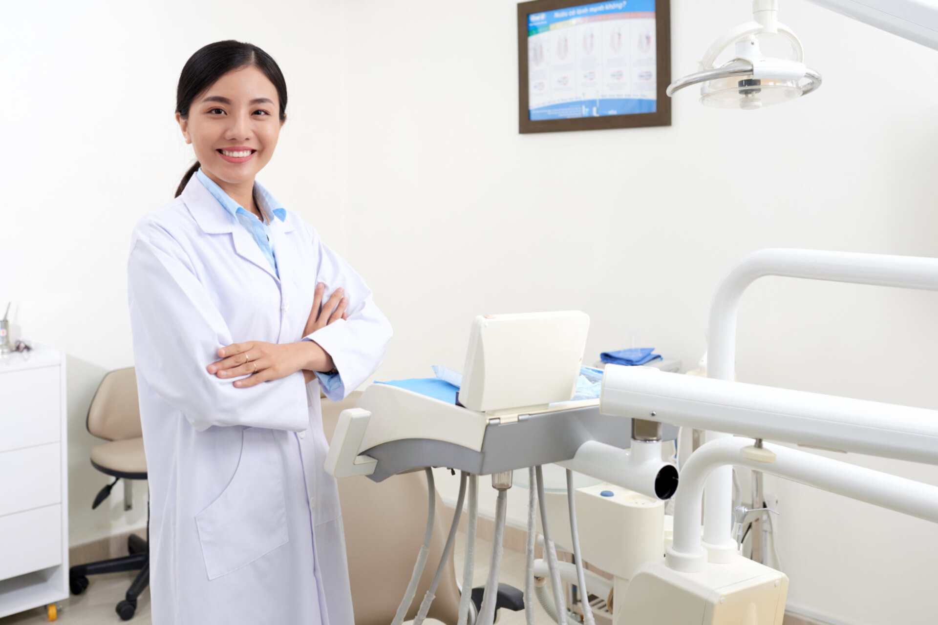 asian female dentist in white coat posing in clinic next to equipment